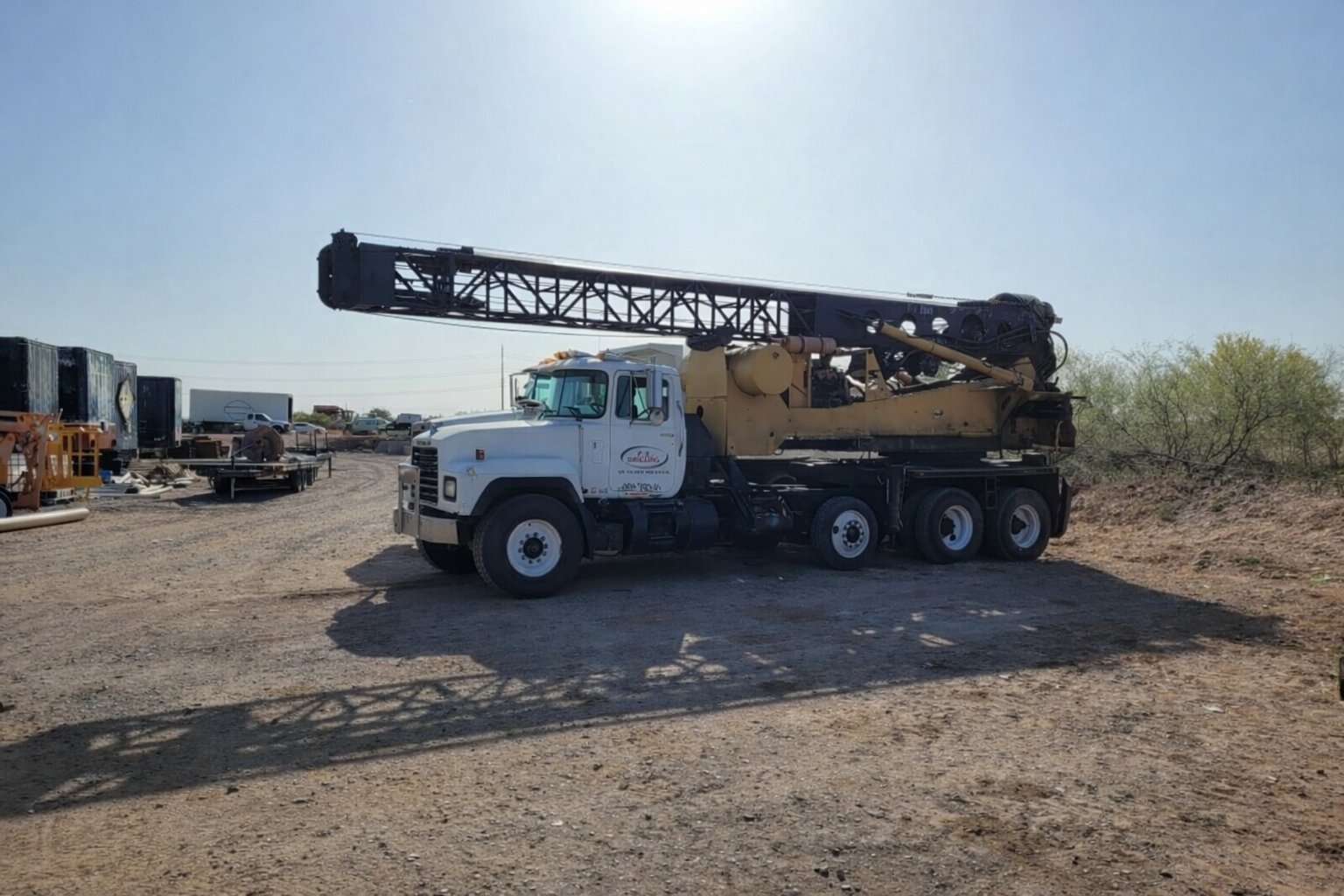 White and tan truck-mounted crane parked in an industrial yard under clear blue sky