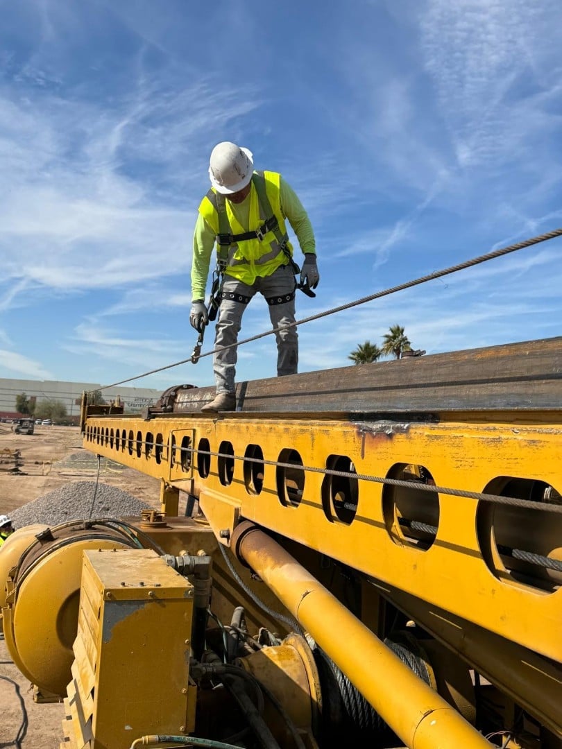 Construction worker in safety gear walking on yellow industrial beam against blue sky